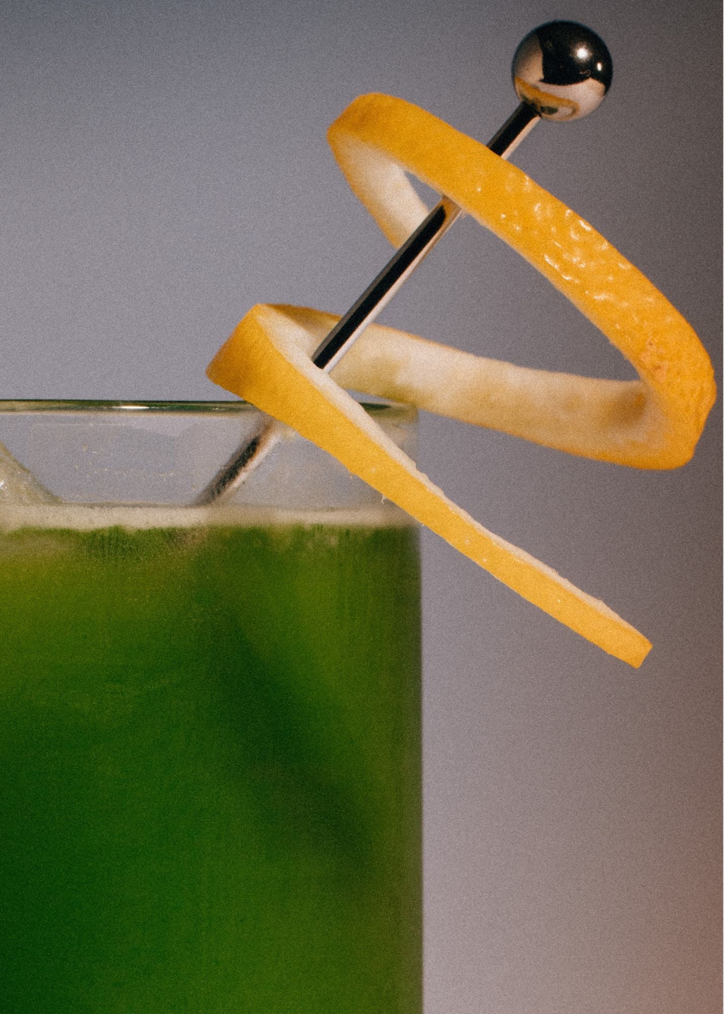 Close-up of a green cocktail with an orange twist on a gray background
