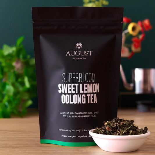 August Superbloom Sweet Lemon Oolong Tea package with a bowl of tea leaves on a wooden surface.
