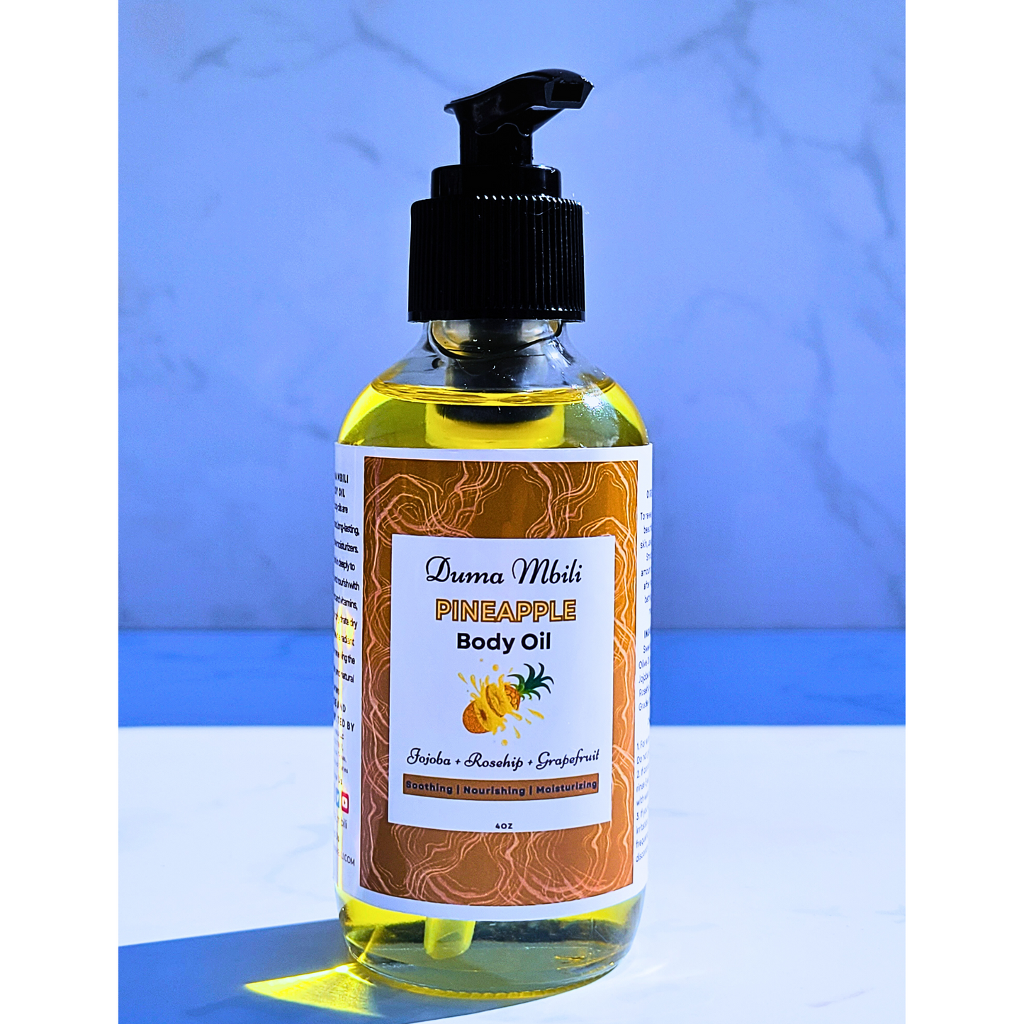 Bottle of pineapple body oil with a pump on a blue and white striped background