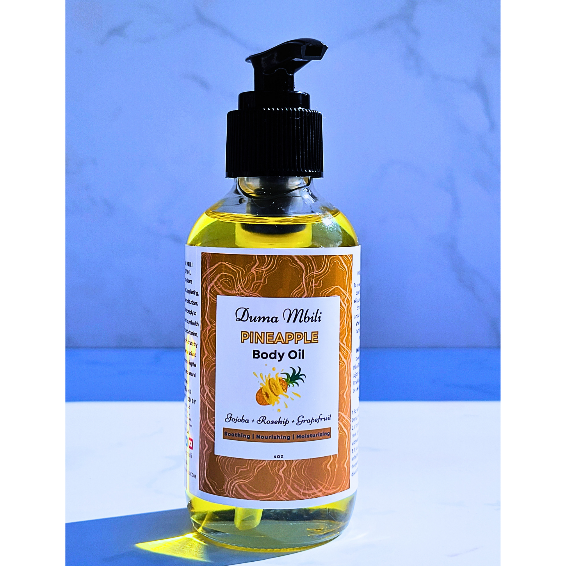 Bottle of pineapple body oil with a pump on a blue and white striped background