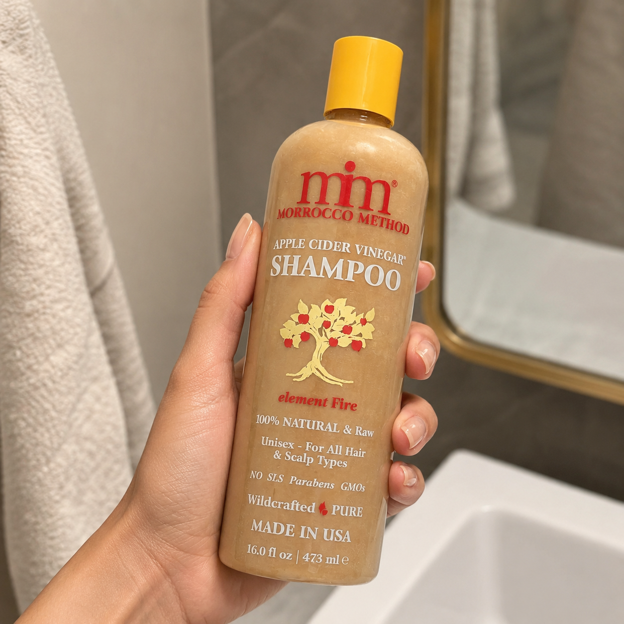 Hand holding a bottle of Morocco Method shampoo with a yellow cap.