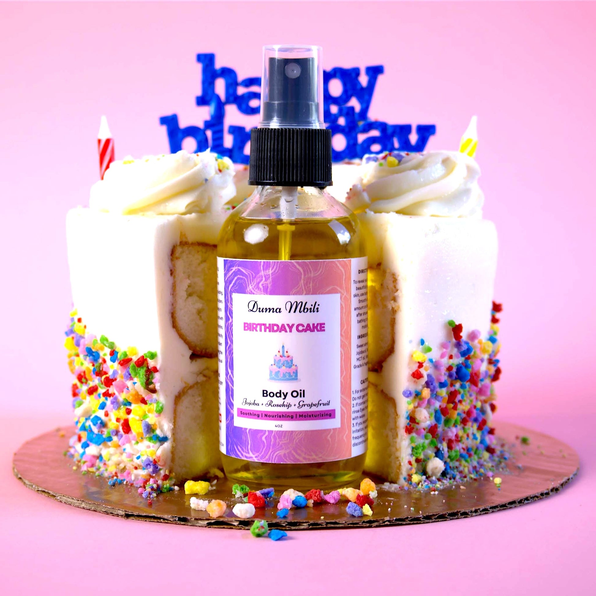 Body oil bottle labeled 'Birthday Cake' with a birthday cake decoration on a pink background