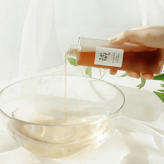 Hand pouring a liquid from a bottle into a glass bowl with a white background