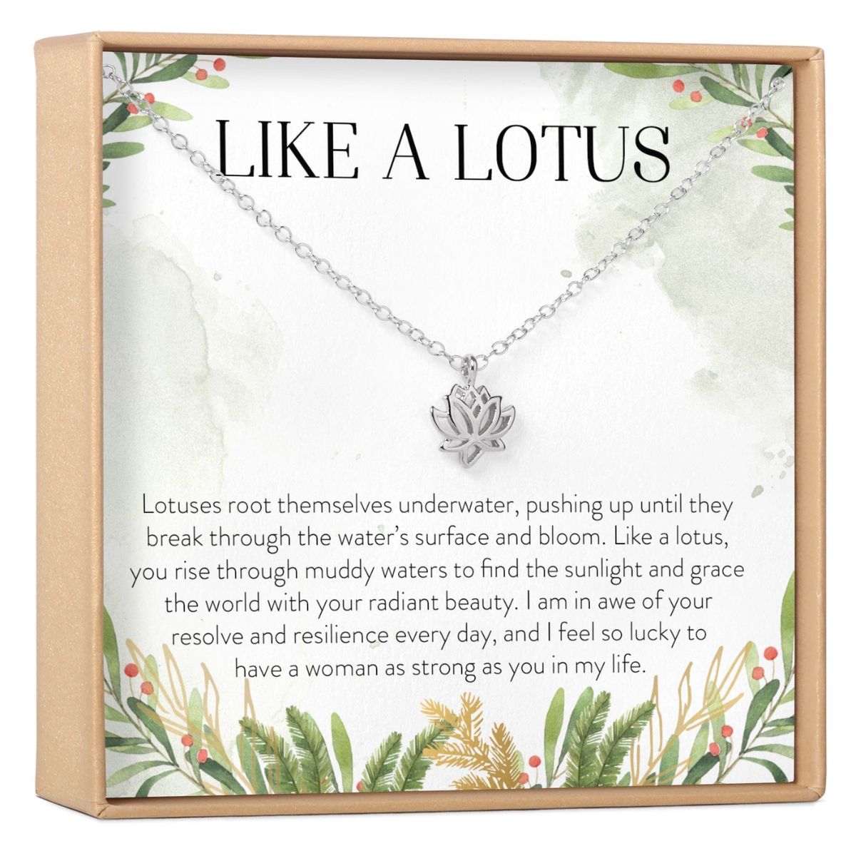 A silver lotus pendant necklace displayed inside a square gift box with a printed message card. The card reads 'LIKE A LOTUS' and includes botanical illustrations and a sentimental quote, with the necklace hanging from a chain above the text.