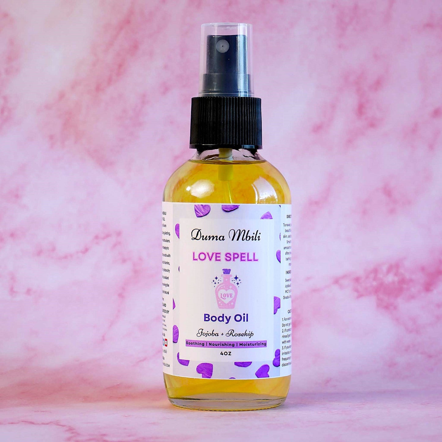 Body oil bottle labeled 'Love Spell' on a pink marble background