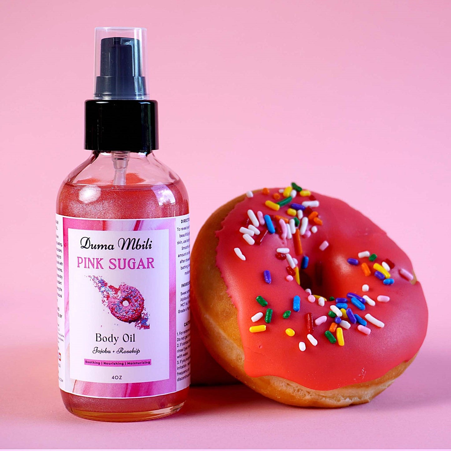 Body oil bottle labeled 'Pink Sugar' next to a pink donut with sprinkles on a pink background
