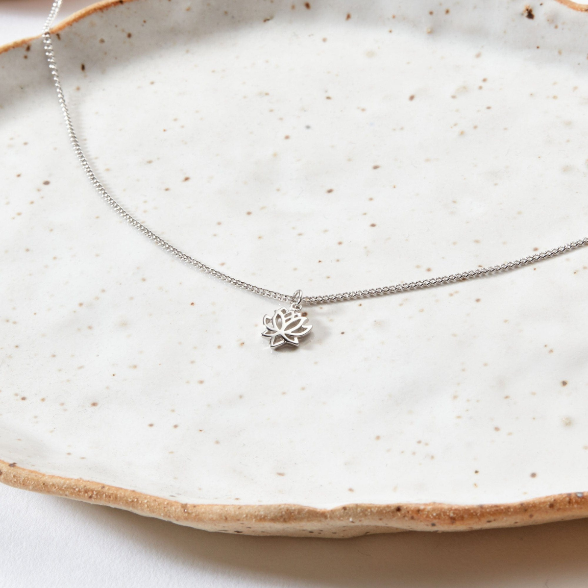Silver necklace with a lotus flower pendant on a textured ceramic plate