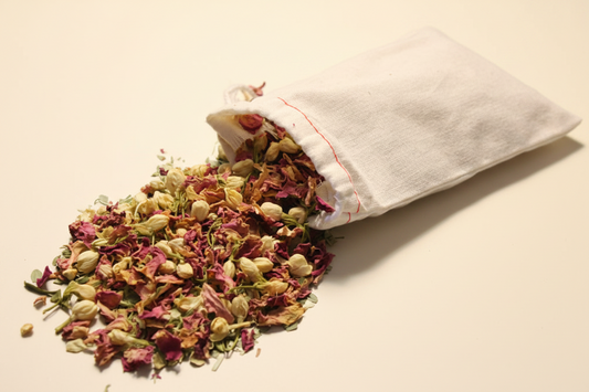 A white fabric pouch tipped on its side with loose dried flower petals and buds spilling out onto a light beige surface.